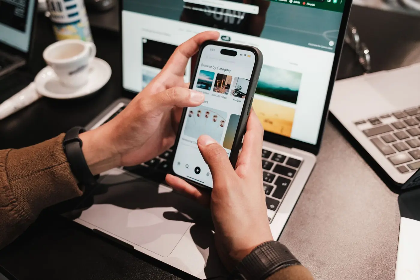 Mains vérifiant les réglages d'un iPhone d'occasion devant un ordinateur portable